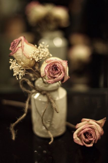 three pink roses in a white vase on a black table with twine and rope