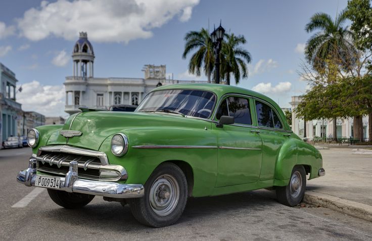 an old green car is parked on the street