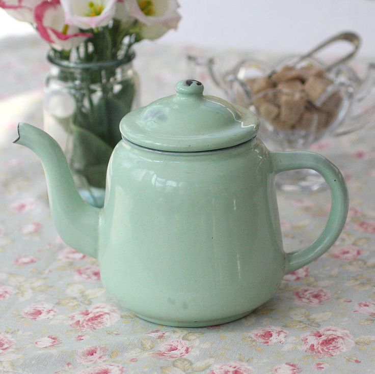 a green teapot sitting on top of a table next to a vase filled with flowers