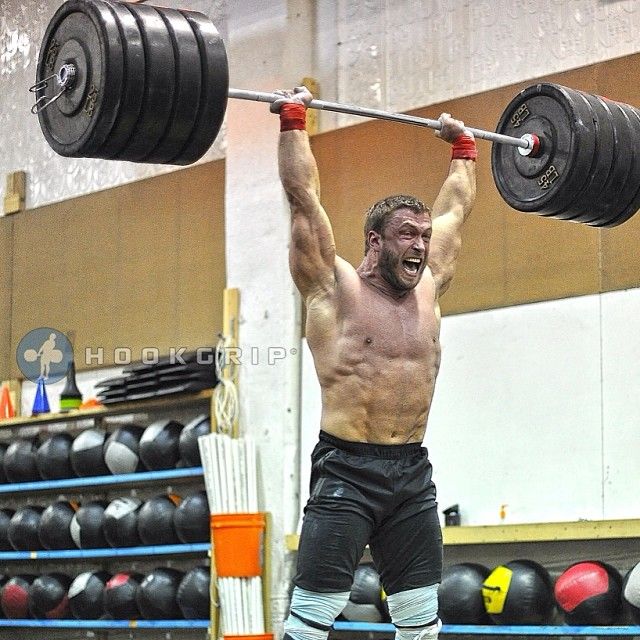 a shirtless man lifting a barbell in a gym with his hands behind his head