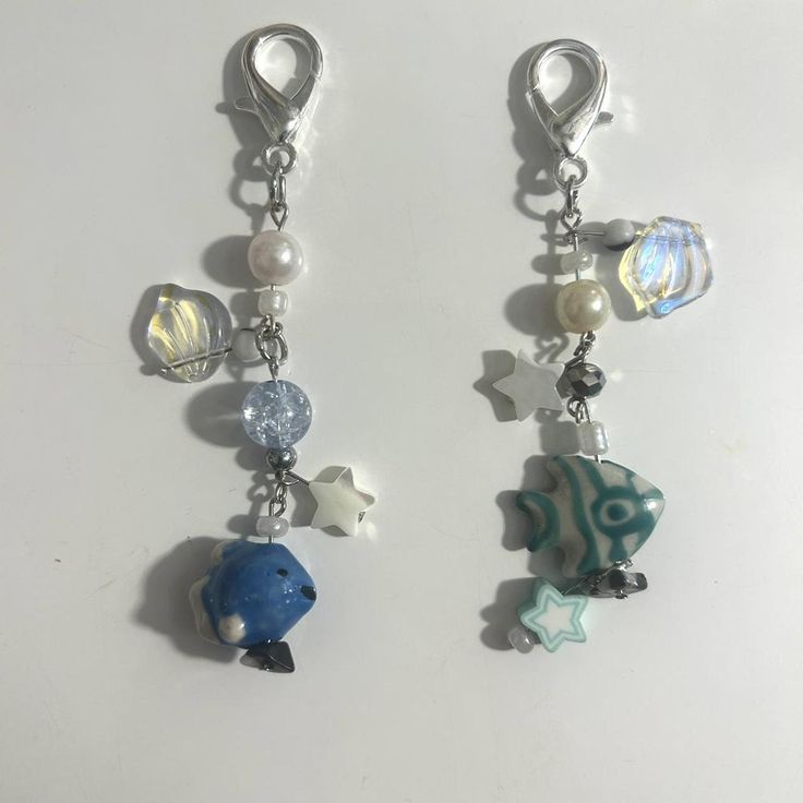 two key chains with charms attached to them on a white surface, one has a fish and the other is a star