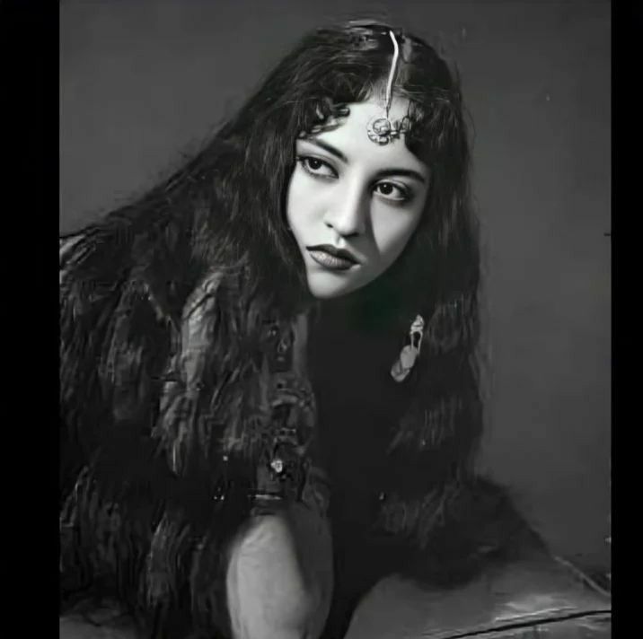 an old black and white photo of a woman with long hair wearing a feathered jacket