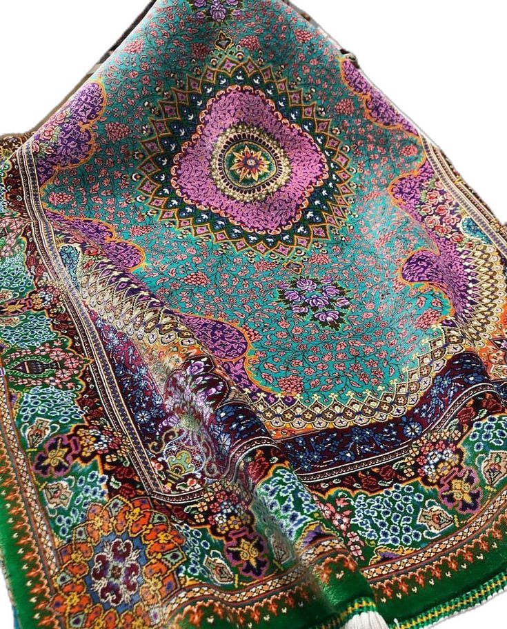 a green and purple scarf with an intricate design on it's edges, folded up to the side