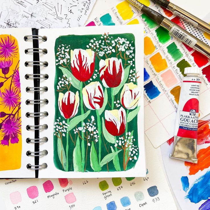 an art journal with watercolors and flowers on it, surrounded by paintbrushes