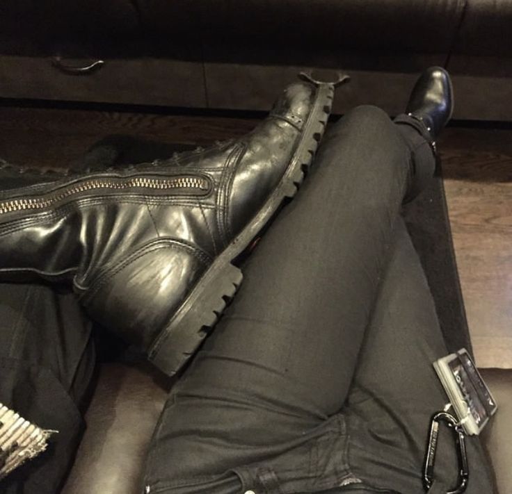 a woman laying on the floor with her legs crossed and wearing black boots, holding a cell phone