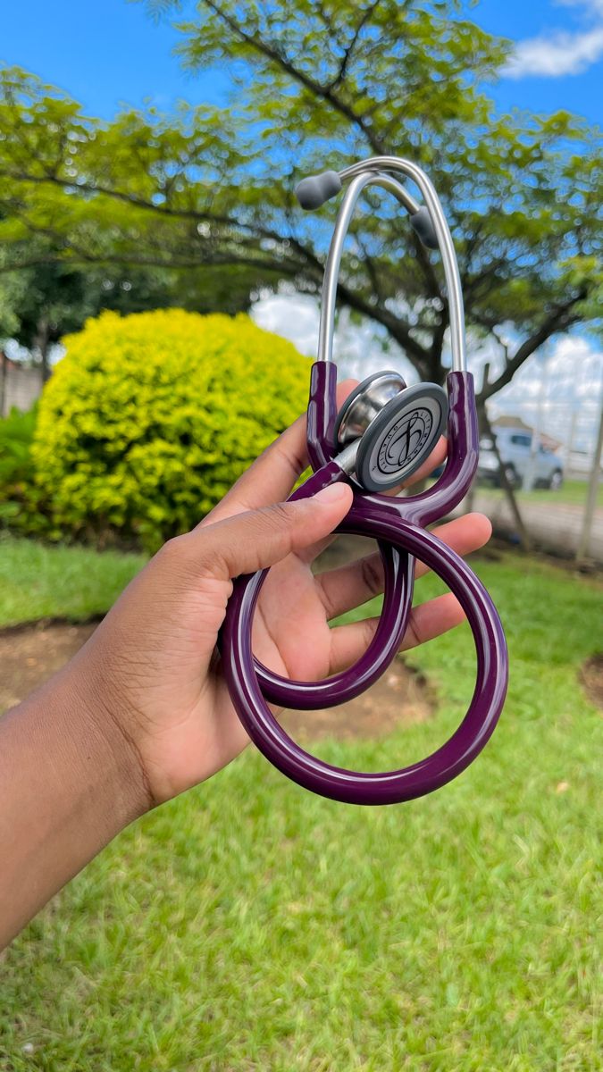 a hand holding a purple stethoscope in front of a green lawn and trees