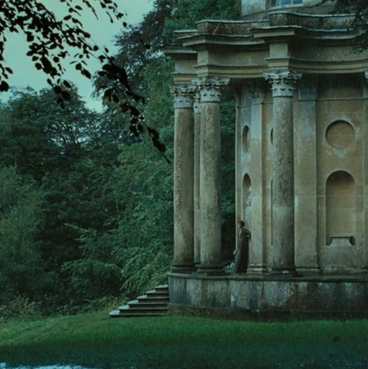 an old building sitting in the middle of a lush green forest next to a body of water