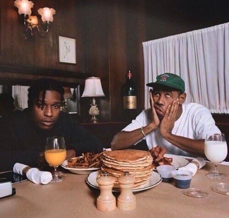 two men sitting at a table with plates of food and drinks in front of them