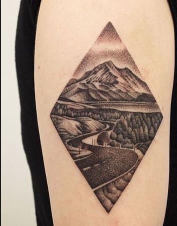 a black and white photo of a diamond shaped tattoo on the right upper arm, with mountains in the background