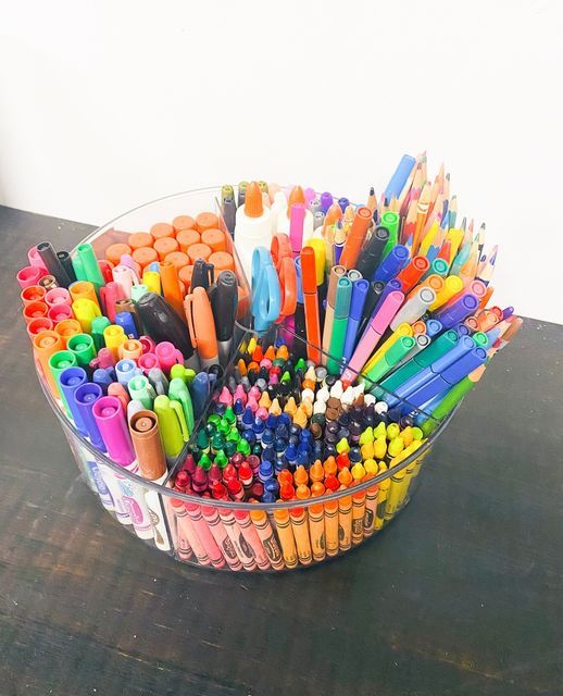 a glass bowl filled with lots of different colored crayons and markers on top of a wooden table