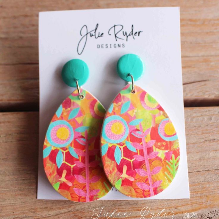 a pair of earrings with colorful designs on them sitting on top of a wooden table