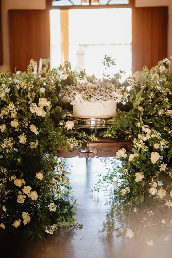 the wedding cake is surrounded by greenery and white flowers at the end of the aisle