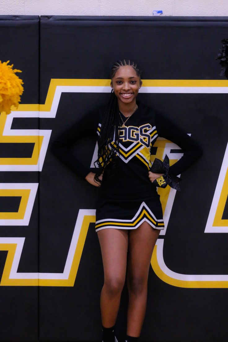 a cheerleader posing for the camera in front of a wall with yellow pom poms