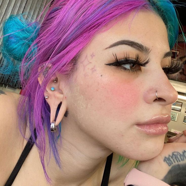 a woman with pink and blue hair has piercings on her ears while looking at the camera