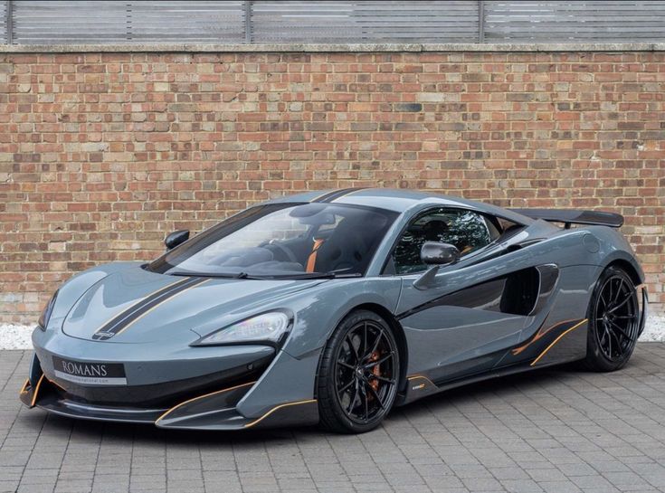 a grey and orange sports car parked in front of a brick wall