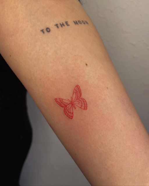 a small red butterfly tattoo on the arm