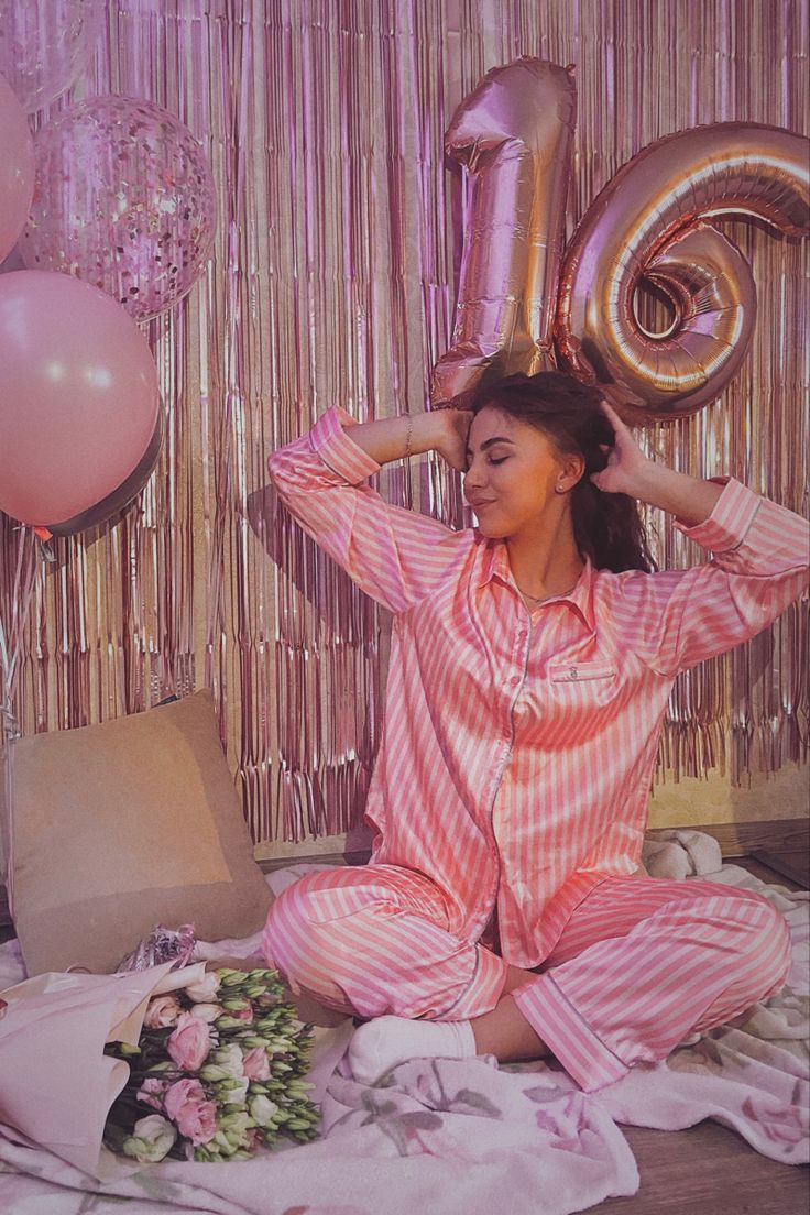 a woman sitting on the floor in pajamas with balloons and streamers around her head