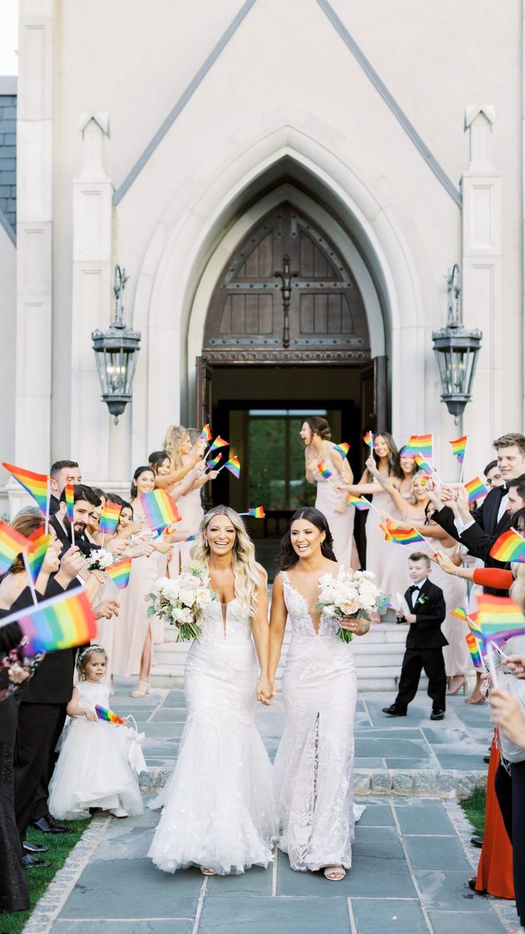 two brides are walking down the aisle with their rainbow flags