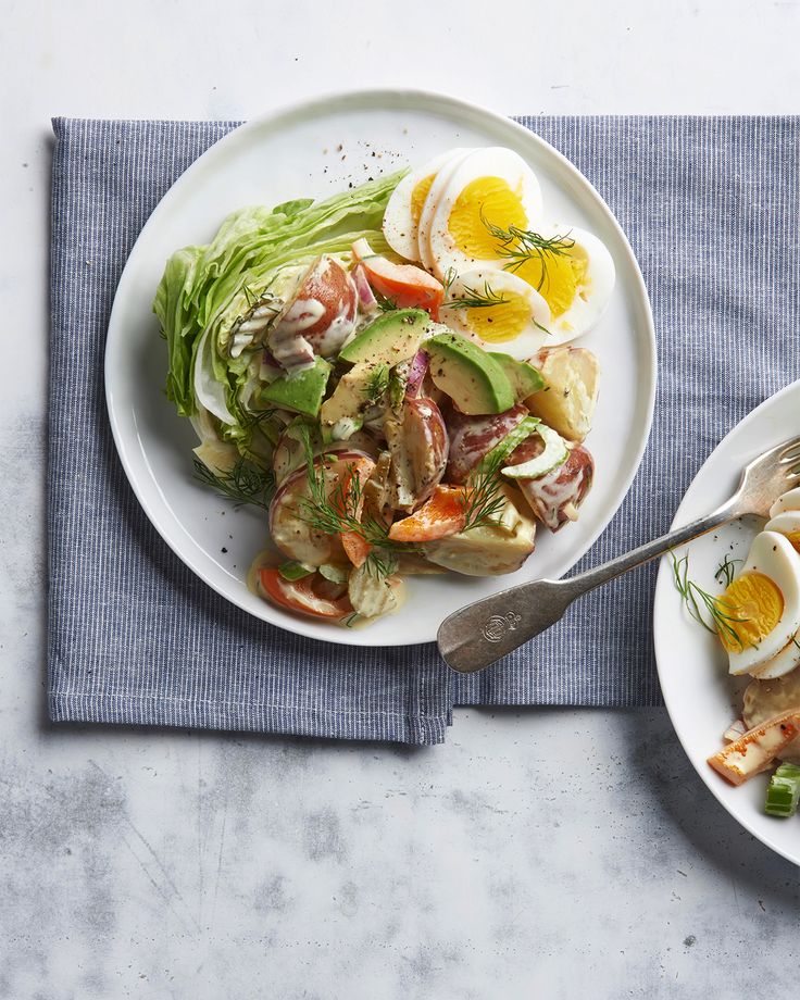 two white plates with food on them sitting on a blue napkin next to a fork and knife