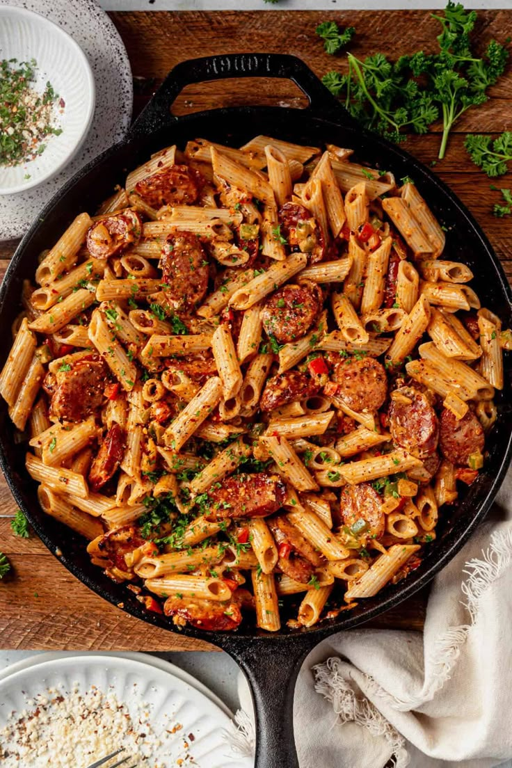 a skillet filled with pasta, sausage and parmesan cheese on a wooden table