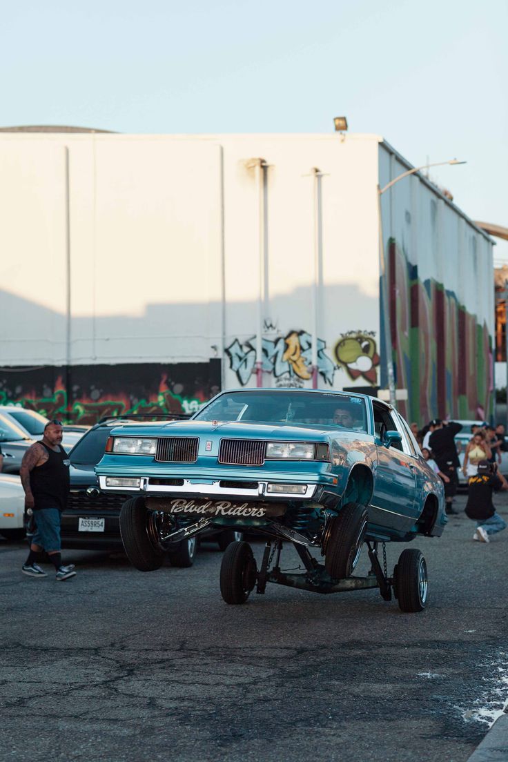 an old car is parked in the parking lot with other cars and people around it