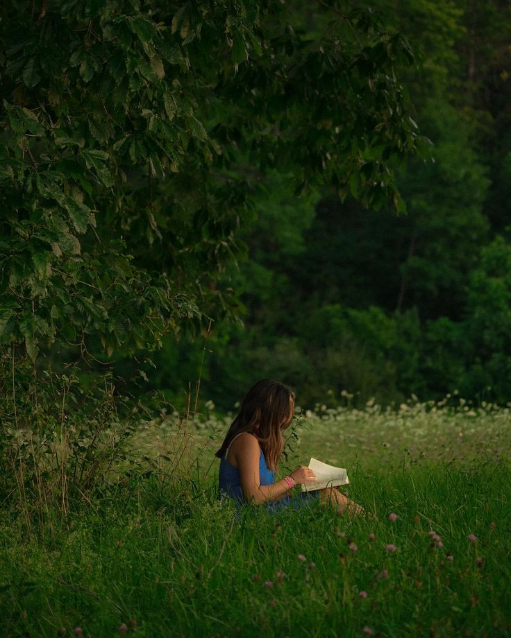 a woman sitting in the grass reading a book