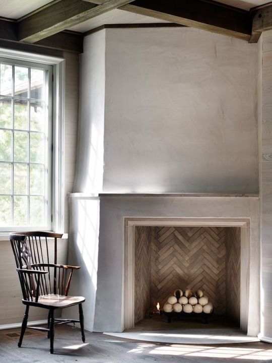 a chair sitting in front of a fire place with logs on the floor next to it