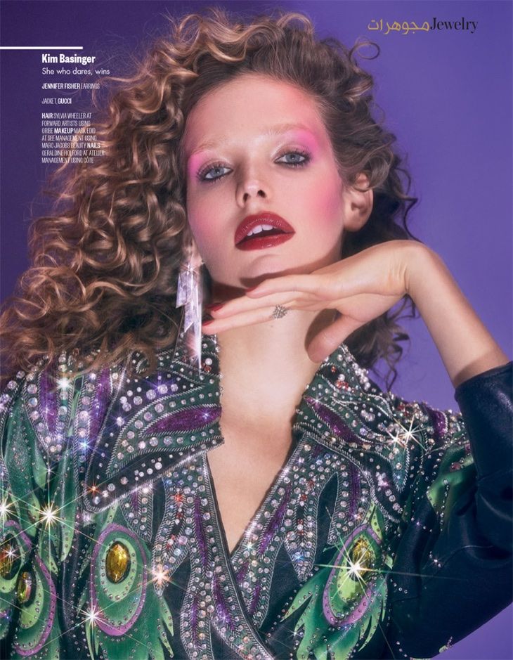 a woman with long curly hair holding a lipstick in her hand and posing for the camera