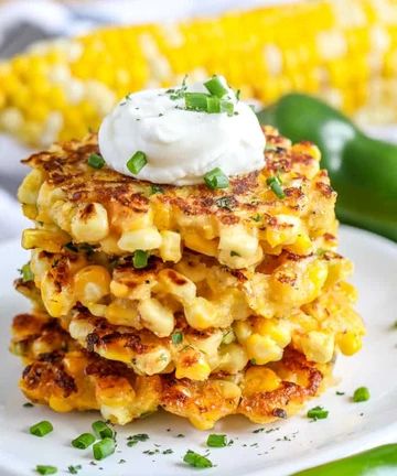 a stack of corn cakes topped with sour cream and green onions on a white plate