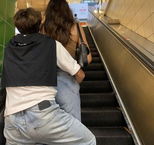 two people on an escalator going down the stairs with their backs to each other