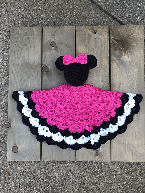 a crocheted minnie mouse hat and dress sitting on top of a wooden plank