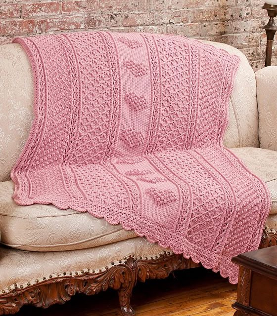 a pink crocheted afghan sits on a couch in front of a wooden table