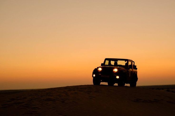 a jeep driving through the desert at sunset