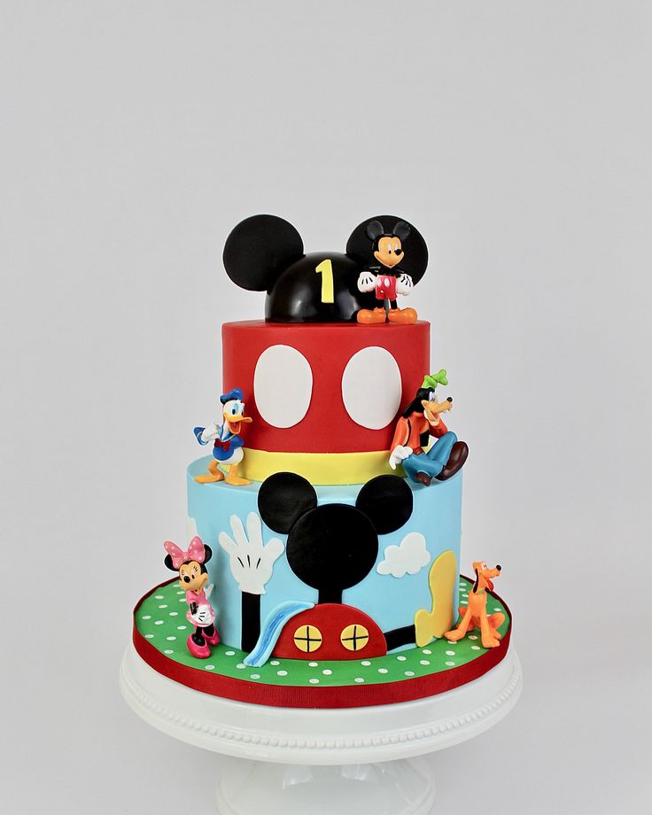 a mickey mouse cake on a plate with the top tier in red and white, topped with figurines