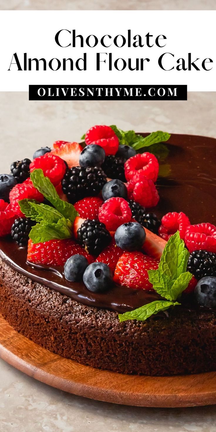 chocolate almond flour cake with fresh berries and mint leaves on top, topped with dark chocolate ganache