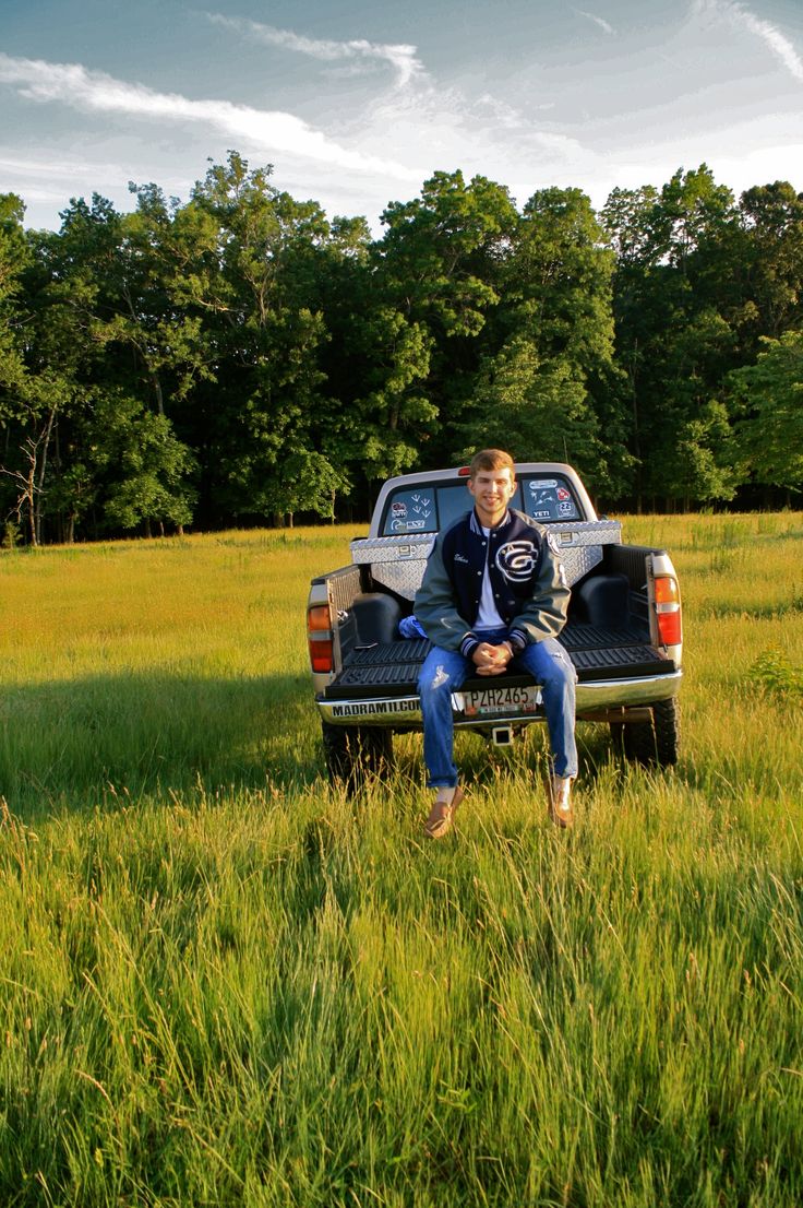 a young man sitting on the back of a pickup truck in a field with tall grass