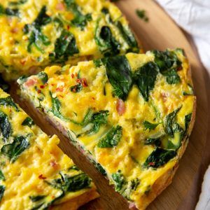 an omelet with spinach and cheese is cut into slices on a cutting board