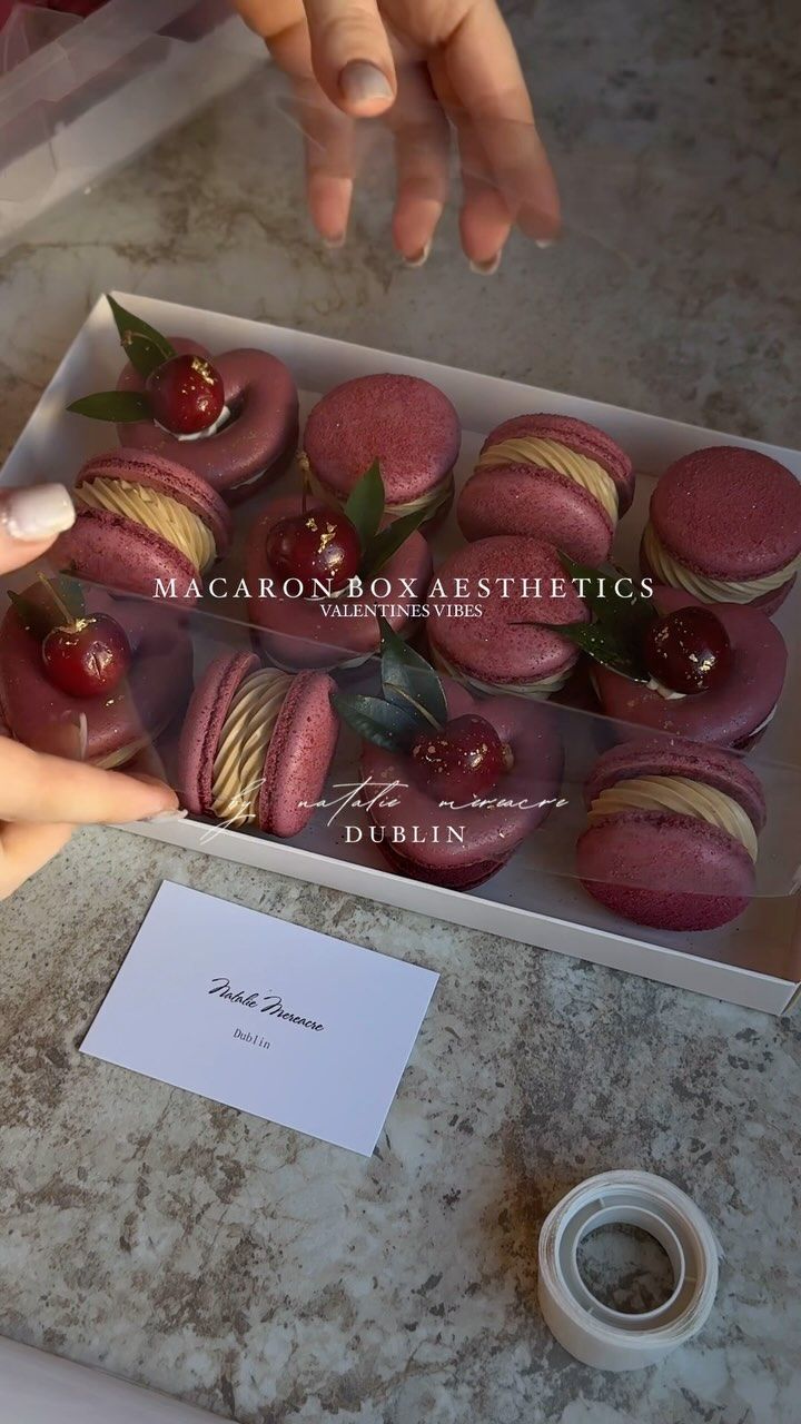 a box filled with macaroons sitting on top of a counter next to a person's hand