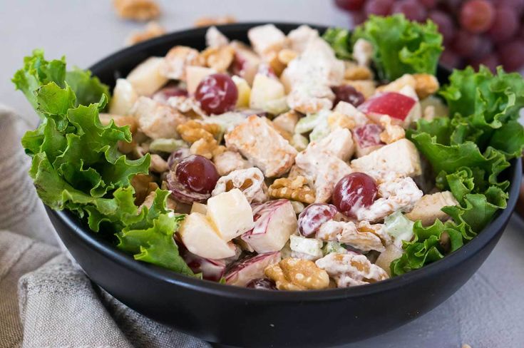 a black bowl filled with salad and fruit on top of a table next to grapes