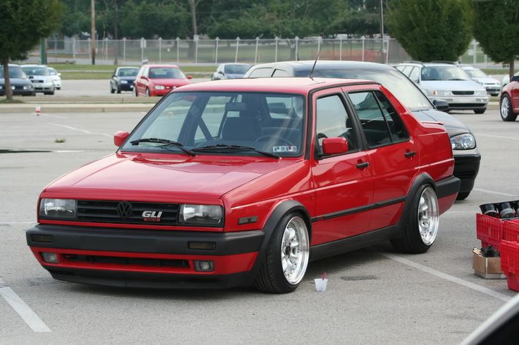 a red car parked in a parking lot next to other cars and boxes on the ground