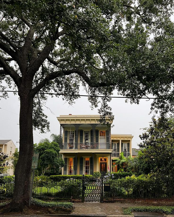 a large yellow house sitting on the side of a road next to a lush green tree