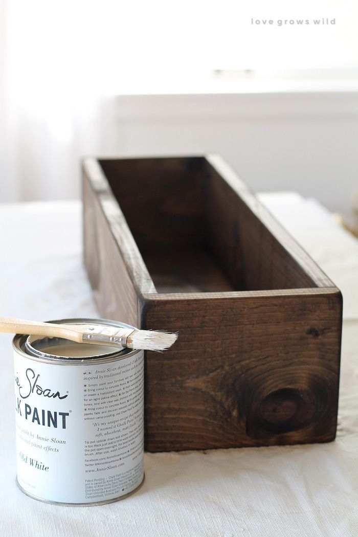 a can of paint sitting on top of a bed next to a wooden box with a brush in it