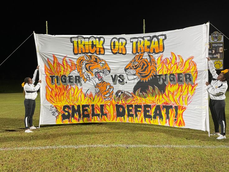 two people holding up a banner that says trick or treat tiger vs tiger on it