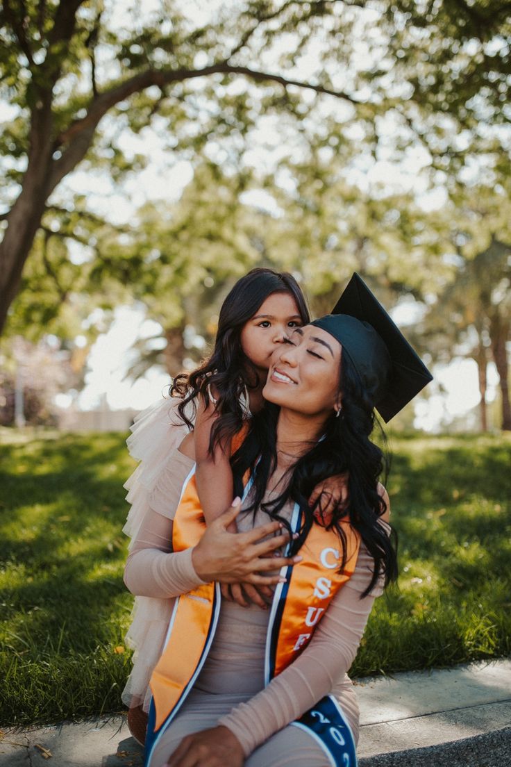 two women in graduation caps and gowns sitting on the ground with their arms around each other