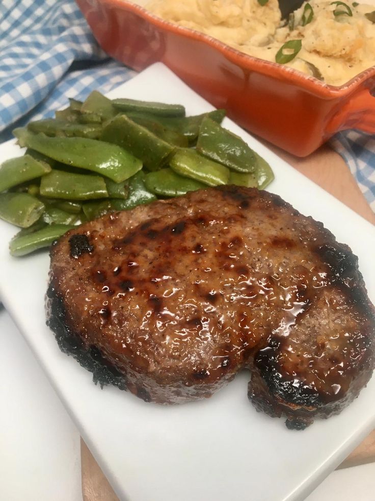 a white plate topped with meat and green beans next to a casserole dish