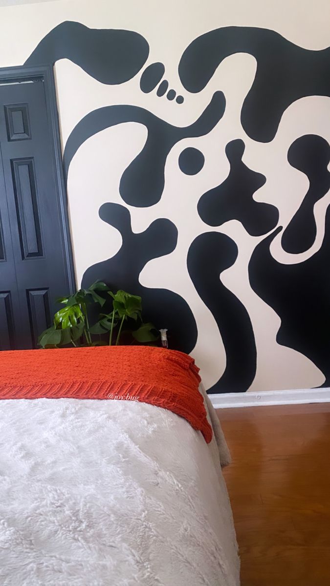 a black and white wall with a plant in the corner next to an orange blanket