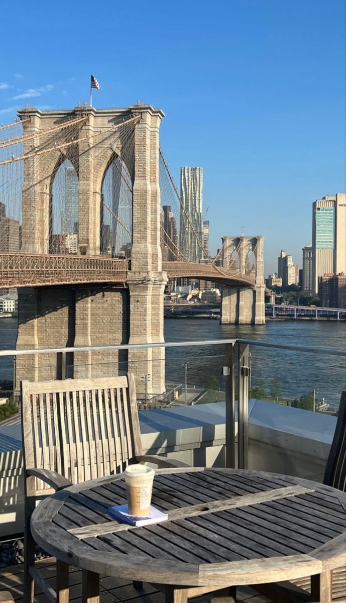 an outdoor table and chairs on a deck overlooking the water with a bridge in the background