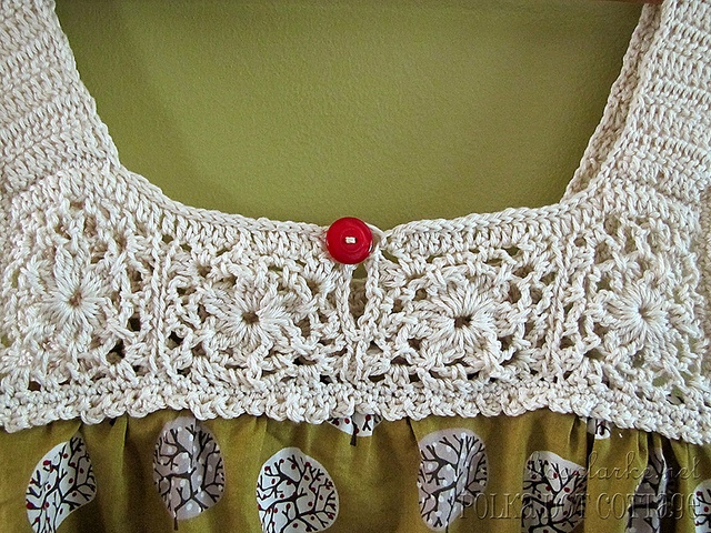 a crocheted top with a red button on it