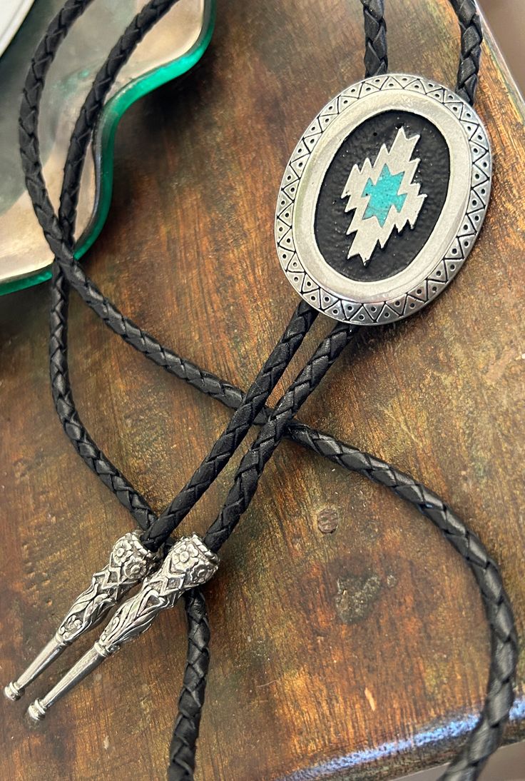 This awesome bolo tie has a southwestern design and real turquoise stone inlay. The cord is genuine leather. Measurements/Sizing Total length of leather is approx. 40 inches1 1/4'' x 2 1/4'' in pendant Handmade Artisan Bolo Ties For Western-themed Events, Adjustable Turquoise Bolo Tie For Rodeo, Adjustable Turquoise Bolo Ties For Rodeo, Artisan Lariat Jewelry For Rodeo, Artisan Bolo Ties With Adjustable Length, Artisan Turquoise Bolo Ties With Concho, Western Style Turquoise Bolo Tie For Western-themed Events, Handmade Southwestern Turquoise Bolo Ties, Adjustable Turquoise Bolo Ties For Western-themed Events