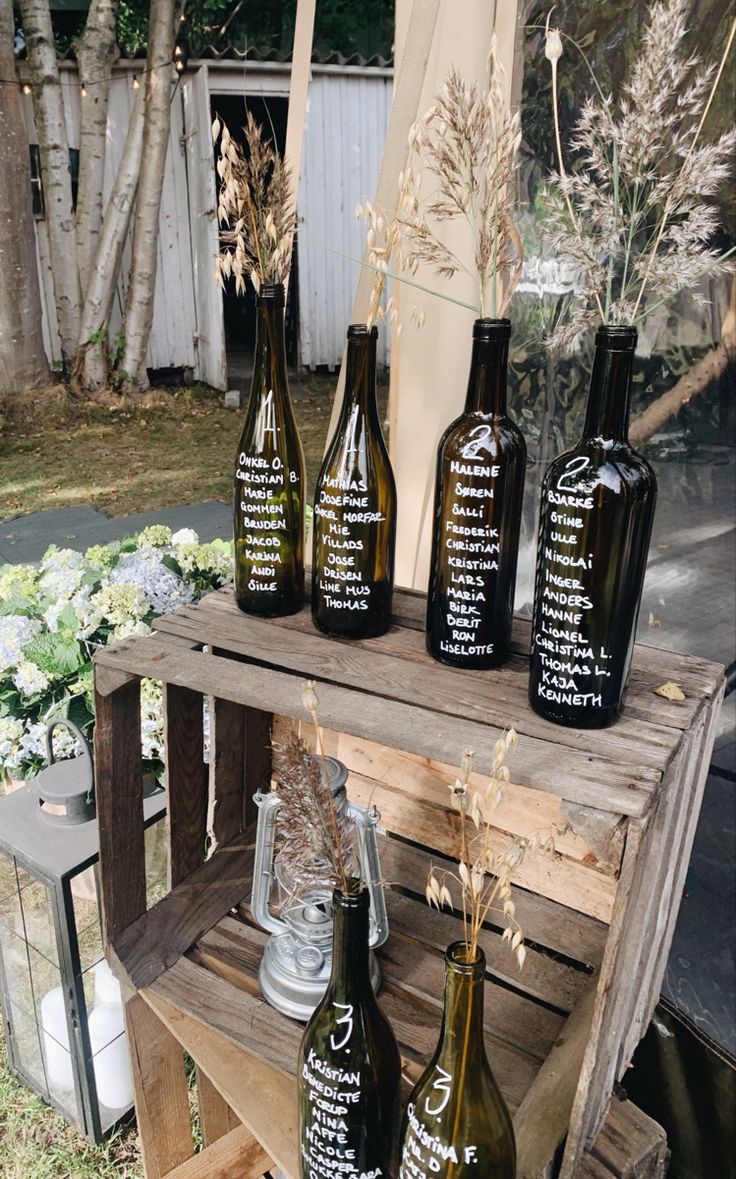 four wine bottles sitting on top of a wooden crate next to flowers and plants in vases